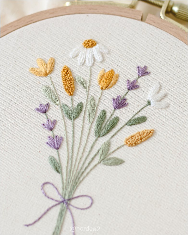 Bastidor com flores brancas, amarelas e lilases bordadas à mão.
